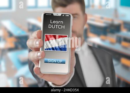 Online concept learn Dutch language with a person showing e-learning app on mobile phone with the flag of Netherlands Stock Photo