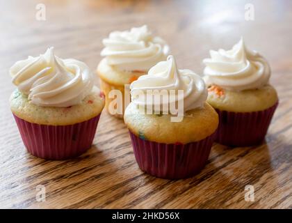 Four mini spring cupcakes on a rough wooden table.  White frosting with no sprinkles. Stock Photo