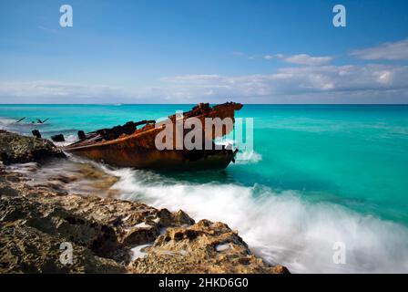 A wave rolls in past the rusting hull and bow of the Gallant Lady shipwreck before breaking on the rocky coastline, North Bimini, Bahamas Stock Photo