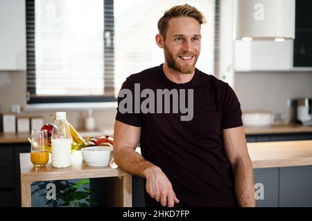Smiling attractive young man standing at the kitchen counter at home Stock Photo