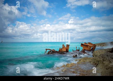 Waves break around the rusting hull of the Gallant Lady shipwreck on a cloudy day with blue sky, North Bimini, Bahamas Stock Photo