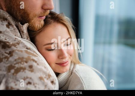 Beautiful happy couple hugging while standing near window indoors Stock Photo