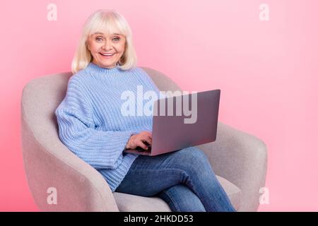 Portrait of attractive cheerful grey-haired woman using laptop watching movie film isolated over pink pastel color background Stock Photo