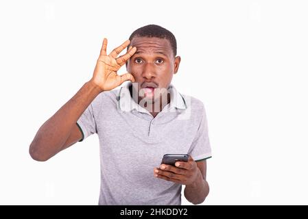 young man holding mobile phone, looking surprised, with hand on face. Stock Photo