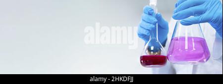 Banner with chemist holding an Erlenmeyer or conical glass flask for titration with bright liquids with copy space. Modern analytical chemistry laboratory Stock Photo