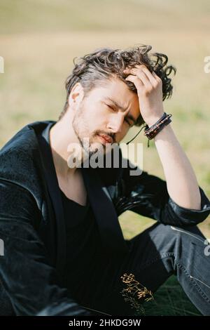 Young man sitting on the grass touching his hair with his hand Stock Photo