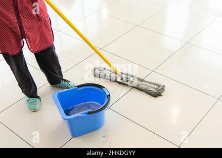 Cleaning lady washes the floor from the tiles in the mall. Woman with mop wiping the floor. Stock Photo