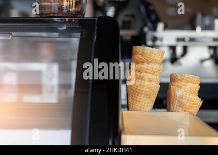 Many empty baked waffle cones and paper cups for ice cream stacked at display counter window of street food takeaway cafe window. Sweet desserts and Stock Photo