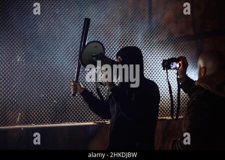 Masked rebel with bat and megaphone. Journalists are making pictires Stock Photo