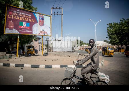 Maiduguri, Borno State, Nigeria. 29th Nov, 2021. A man cycles past an election billboard in Maiduguri, the capital of Borno State.Islamic militant group Boko Haram, and more recently a faction called ISWAP, have been waging an insurgency in northeast Nigeria for more than a decade. (Credit Image: © Sally Hayden/SOPA Images via ZUMA Press Wire) Stock Photo