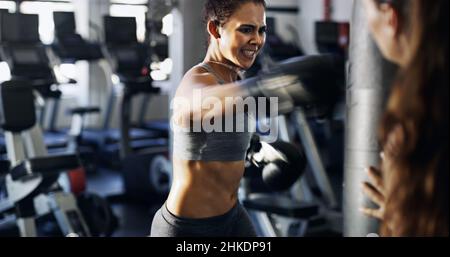 Give it all youve got. Cropped shot of a young female boxer working out on a punching bag with her trainer in the gym. Stock Photo