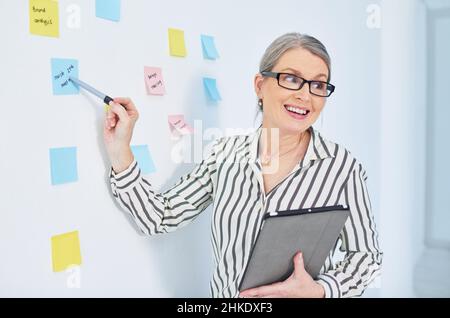 She always presents the best plans. Shot of a mature businesswoman giving a presentation with notes on a wall in an office. Stock Photo