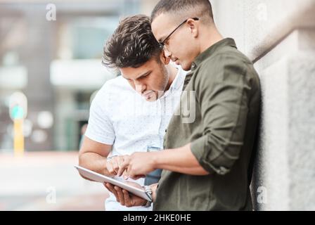 Success starts out small. Shot of two young businessmen using a digital tablet together against an urban background. Stock Photo