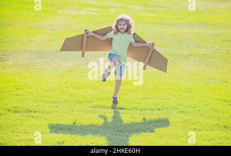 Child playing with toy wings in park on green grass background. Stock Photo