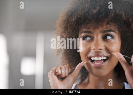 She's big on dental hygiene. Shot of a young woman flossing her teeth in the mirror. Stock Photo