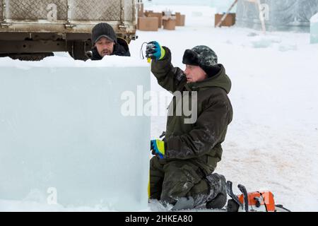 Workers installers mark the ice block on the assembly site of the ice city using a tape measure Stock Photo