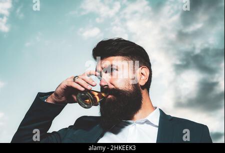Handsome pensive man is holding a glass of whiskey and looking away outdoors. Stock Photo