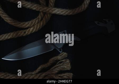 Tactical folding knife for survival, active lifestyle and recreation, on rope background and dark background Stock Photo