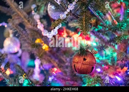 Close up of a red, glittery bell hanging on a Christmas tree with the rest of the ornaments and tree out-of-focus with negative space. Stock Photo