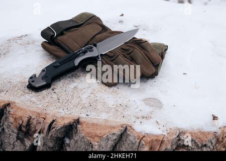 Tactical gloves and a folding knife in the snow Stock Photo