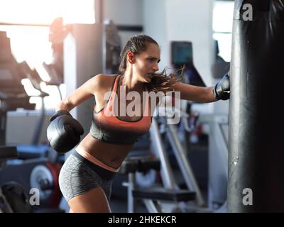 Southpaw elegance. Shot of a young female boxer working out on a punching bag in the gym. Stock Photo