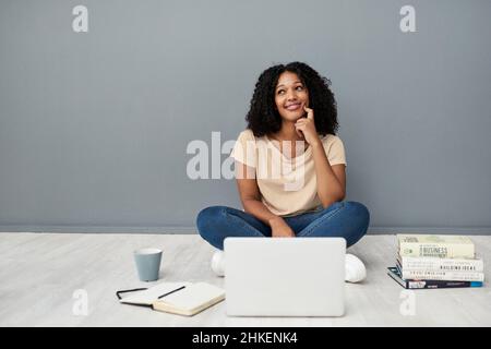 University days gone virtual. Studio shot of a young woman using a laptop while completing her studies against a gray background. Stock Photo