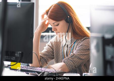 Beautiful young Caucasian red hair girl with hands on head dressing casual with headache or migraine working in the office or class at the desk Stock Photo