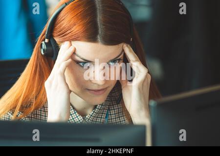 Beautiful young Caucasian red hair girl with hands on head dressing casual with headache or migraine working in the office or class at the desk Stock Photo