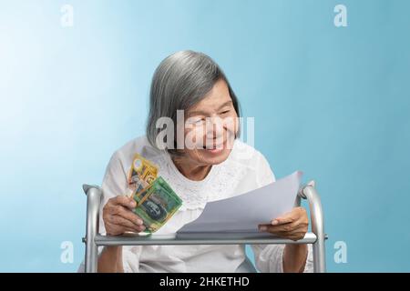 Elderly asian woman smile while reading letter and hold australian banknote on walker. Stock Photo