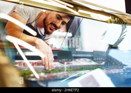 Young man butcher arranging meat products in display case of butcher shop Stock Photo