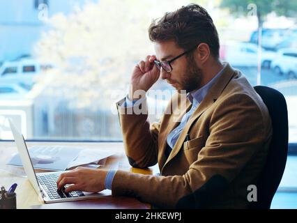 Another day in the office. Cropped shot of a handsome businessman working on a laptop while sitting at his desk in the office. Stock Photo