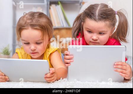 Two children lie on the floor and carefully look at the tablets Stock Photo