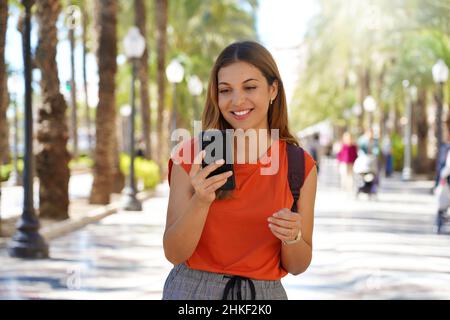 Hispanic young woman laughing and texting on her mobile phone walking outdoors Stock Photo