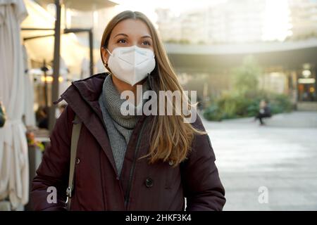 Happy young woman using medical face mask over city background looking to the side and staring away thinking Stock Photo