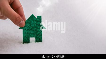 House icon with hand on snow texture nature background as symbol of mortgage, dream house on nature background and space for your text. Stock Photo