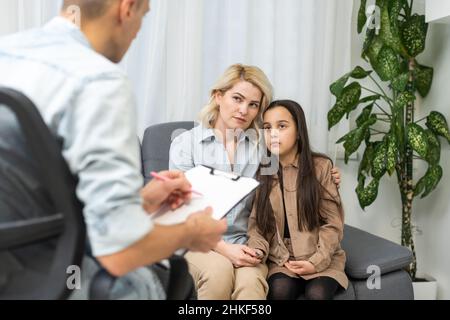Female psychologist counseling parent. Serious single mom and sad unhappy child sitting on sofa and discussing social behaviour, ADHD disorder Stock Photo