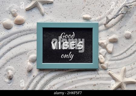 Background with white sand with shells, starfish. Good vibes only text on blackboard in mint green frame. Stock Photo