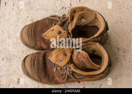 Pair of men's brown work boots - worn out splits and holes beyond repair. From above, on pavement. Queensland Australia. Stock Photo
