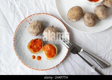 Potatoes on a white plate with red pepper and paprika sauce with cutlery. A traditional Canarian dish is papas arrugadas. Vegetables are boiled in wat Stock Photo