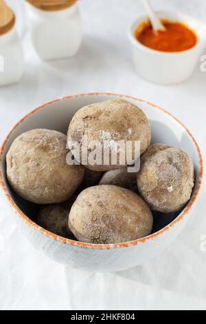 Potatoes on a white plate with red sauce on a white tablecloth. A traditional Canarian dish is papas arrugadas. Vegetables are boiled in water with a Stock Photo