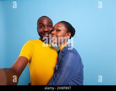 POV of people in relationship smiling in front of camera, taking pictures together in studio. Cheerful couple using phone in hand to take selfies and share romance. Partners hugging each other Stock Photo