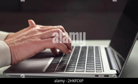 Elderly woman works at laptop typing quickly on keyboard Stock Photo