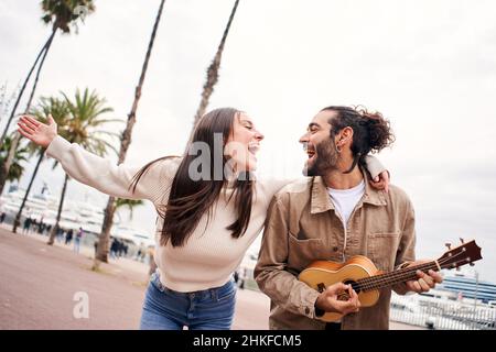 Happy couple singing and dancing playing the ukulele outdoors at the city. Stock Photo