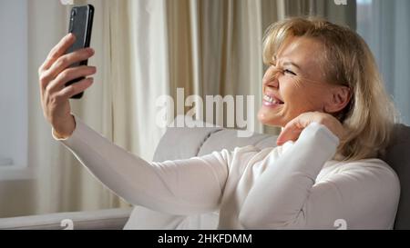 Elderly blonde woman takes selfies using cellphone Stock Photo