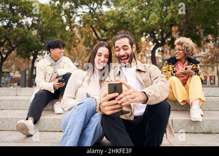 Smiling couple using smartphone and laughing outdoors. People and technology having fun. Stock Photo