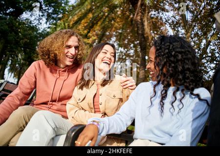 Happy Caucasian couple laughs in the park with an African-American friend Stock Photo
