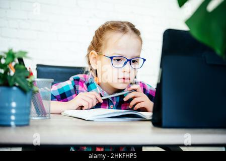 Primary school girl in eyeglasses at the table using her tablet during covid lockdown, distance education for children Stock Photo