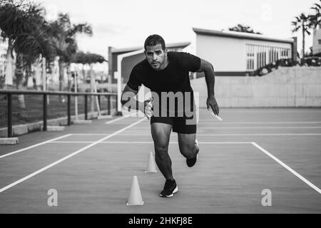 Hispanic man doing speed and agility cone drills workout session outdoors - Focus on man face - Black and white edition Stock Photo