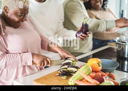 Happy black family cooking inside kitchen at home - Focus on left hand holding knife Stock Photo