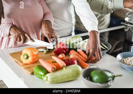 Black family cooking inside kitchen at home - Focus on left hand holding knife Stock Photo
